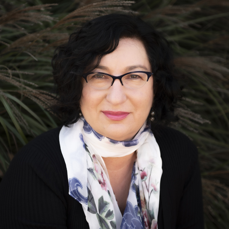 People stand on either side of tables lined with informational materials under a white event tent, talking and smiling.